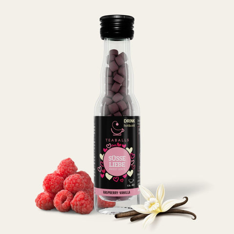 TEABALLS - Vanille & Himbeere - Sommergenuss tea blend in a clear glass teapot with fresh raspberries and vanilla pods on a wooden table